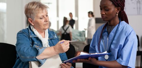 African american nurse explaining sickness treatment to elderly patient African american nurse explaining sickness treatment to elderly patient putting her to sign medical document in hospital waiting room area during clinical consultation. Healthcare support service