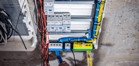 A male electrician works in a switchboard with an electrical connecting cable. A male electrician works in a switchboard with an electrical connecting cable, connects the equipment with tools, top view.