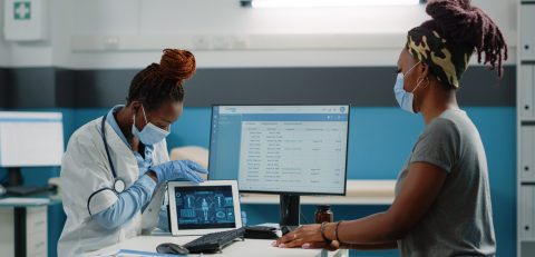 Medic and patient looking at human body analysis Medic and patient looking at human body analysis for osteopathy diagnosis in cabinet. Doctor with skeleton scan on digital tablet talking to young woman about osteoporosis treatment.